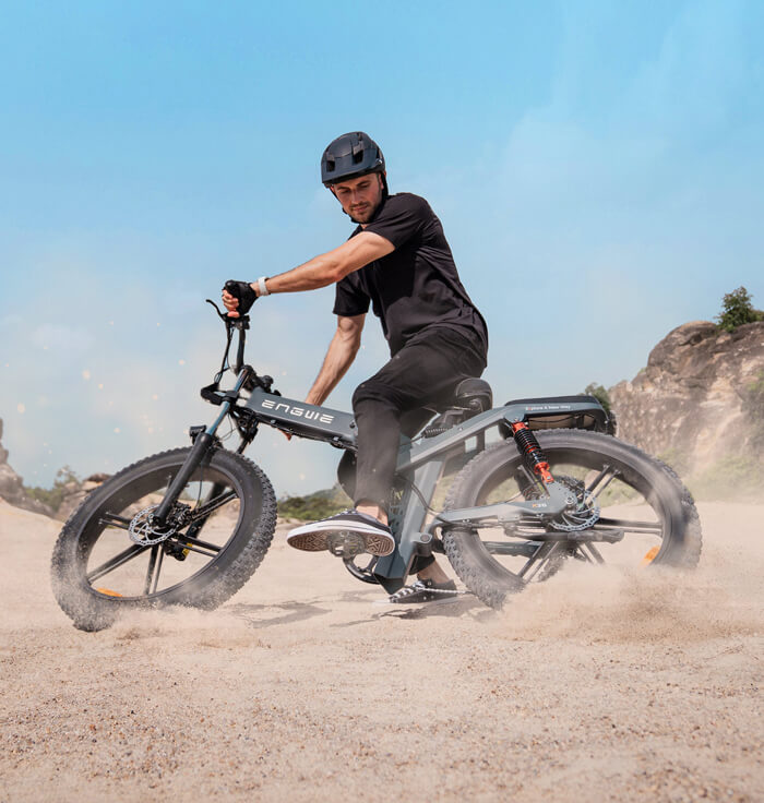 a man in black rides an engwe x26 e-bike on the sand